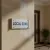 Plaque de porte « LOCAL SONO » fixée sur un mur beige d'un couloir, près d'une porte