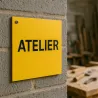 Panneau personnalisé carré en PVC rigide jaune, vissé sur le mur d'un atelier de menuiserie